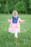 A little girl 3 years old walks in the park in a dress and a pink sweater. photo