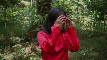 retrato do uma lindo ásia mulher dentro uma vermelho Jaqueta em pé dentro a floresta e sorridente às natureza video