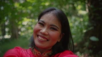 Portrait of a beautiful Asian woman in a red blouse taking a selfie inside the rainforest video