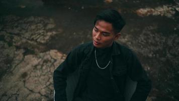 Portrait of a young Asian man in a black jacket and chain sitting on a chair when relaxing video