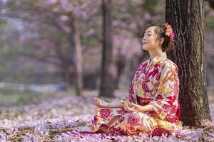 japonés mujer en kimono vestir es haciendo meditación debajo sakura árbol durante Cereza cierne temporada para interior paz, atención plena y zen práctica foto