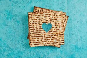 Pesach celebration concept - Jewish holiday Pesach. Matzah squares stacked in a square on blue background. Heart carved in matzah. Flat lay photo