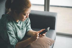 hand of asian woman using smartphone on sofa relaxing and shopping online working from home.use of technology for e-learning,social media,e-commerce photo