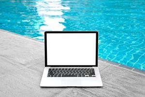 ordenador portátil con blanco pantalla para creativo diseño en piso cerca nadando piscina borde antecedentes. computadora cuaderno con monitor recorte camino para presente aterrizaje página diseño. ordenador portátil computadora burlarse de arriba modelo foto