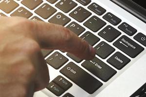 Closeup of laptop computer with forefinger for business concept background. Businesssman hand touching enter button on Laptop keyboard. Computer notebook with man index finger push keypad. photo