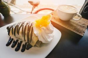 The sweet dessert chocolate banana crepes with gold threads topping and a cup of hot latte coffee. photo