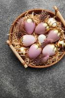 Golden and pink colored eggs and  feathers in wicker plate photo
