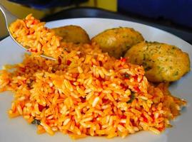 Close up a fork scooping an orange color fried rice in the white plate with blurred Croquette in background photo