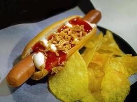 Selective focus of fresh made Hot dog topping with ketchup and mayo with potato chips on paper, fast food, quick meal, high angle view photo