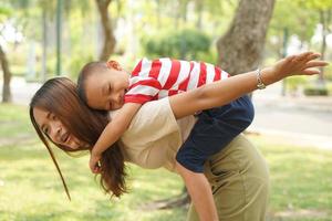 A boy happily rides on his mother's back in the park. photo