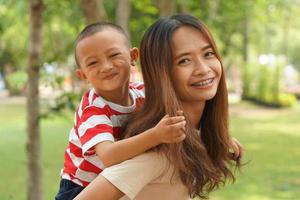 A boy happily rides on his mother's back in the park. photo