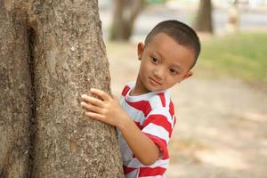 A boy hides behind a tree so his mother can't see photo