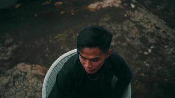 Portrait of a young Asian man in a black jacket and chain sitting on a chair when relaxing video