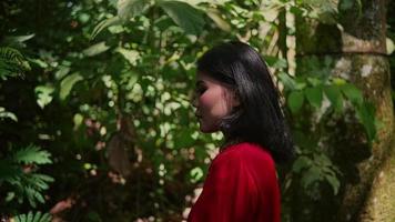 asiático mujer en un rojo seda túnica y con largo negro pelo en pie en el selva video