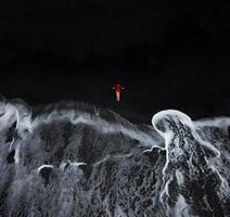 aéreo ver de un niña en un rojo vestir sentado en el playa con negro arena. tenerife, canario islas, España foto