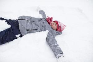 un contento chico mentiras en el nieve y disfruta el clima. foto