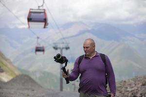 A man is filming a cable car in the mountains with a video camera. A tourist writes a YouTube blog while traveling. photo