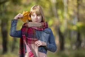 Red-haired little girl with a yellow maple leaf. Child in the autumn park.The concept of the arrival of autumn. photo