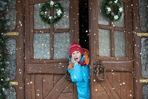 Child boy welcomes guests, surprised, the house is decorated before Christmas. The boy looks out of the Christmas door. photo