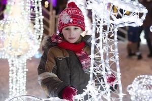 A little boy in a knitted red hat on the background of a Christmas festive urban decor. photo