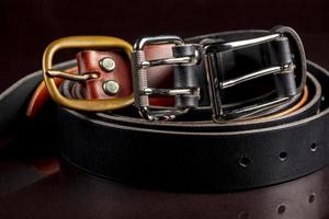 Several leather belts with a metal buckle on a dark background. photo