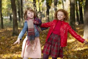 Two girlfriends run through the autumn park. Children play in autumn. photo