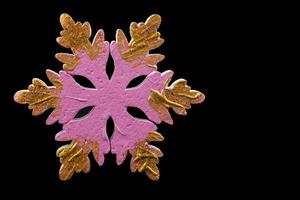 Festive Christmas background. On a black background, a minimalistic pink large snowflake with gold glitter. photo