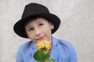 Portrait of a boy in a hat and suit with a rose. Child with flower for mother's day or holiday. Elegant funny man with a flower for a gift. photo