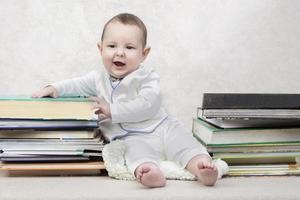 pequeño niño entre libros. contento seis mes antiguo bebé chico en un apilar de libros. el concepto de temprano infancia educación. foto