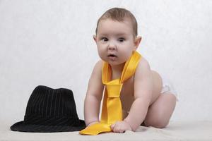 sonriente niño en un retro sombrero y Corbata en un blanco antecedentes. gracioso seis mes antiguo bebé en elegante ropa. foto