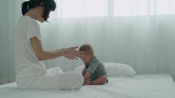 asian mother is training her child to crawl on the bed. The mother is encouraging the child to make an effort to practice her crawling. The concept of development according to age. video