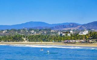 Sun beach cliffs rocks waves palms mountains Puerto Escondido Mexico. photo