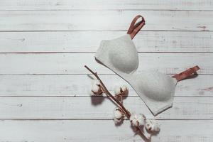 Grey bra with cotton brunch on wooden background, closeup photo