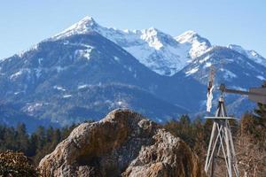 Weather vane by large rock with idyllic snow covered mountain in photo