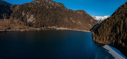 Aerial view of the snow rocky cliffs with forest by the lake. Dramatic and picturesque scene. photo