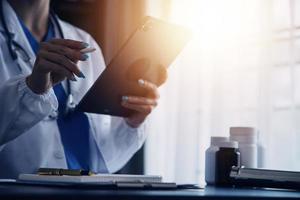 médico trabajando con ordenador portátil computadora y escritura en papeleo. hospital antecedentes. foto