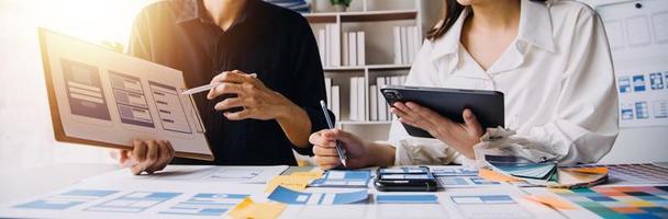 Close up ux developer and ui designer brainstorming about mobile app interface wireframe design on table with customer breif and color code at modern office.Creative digital development agency photo