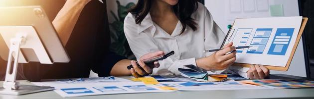 Close up ux developer and ui designer brainstorming about mobile app interface wireframe design on table with customer breif and color code at modern office.Creative digital development agency photo