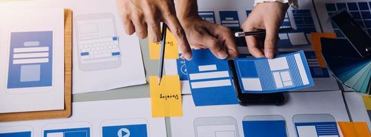 Close up ux developer and ui designer brainstorming about mobile app interface wireframe design on table with customer breif and color code at modern office.Creative digital development agency photo