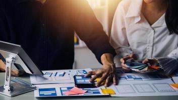 Close up ux developer and ui designer brainstorming about mobile app interface wireframe design on table with customer breif and color code at modern office.Creative digital development agency photo