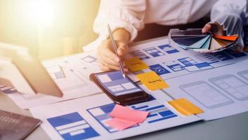 Close up ux developer and ui designer brainstorming about mobile app interface wireframe design on table with customer breif and color code at modern office.Creative digital development agency photo