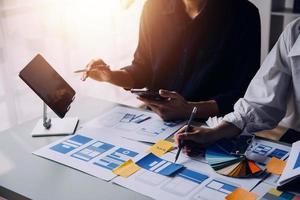 Close up ux developer and ui designer brainstorming about mobile app interface wireframe design on table with customer breif and color code at modern office.Creative digital development agency photo