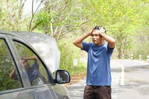 Man looking at a broken car engine on the side of the road photo