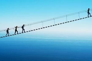 A suspension bridge over a cliff on the background of the sky with people climbing up. Selective focus photo