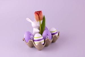 A white ceramic rabbit with a tulip in an egg box, Easter eggs are lying next to it photo