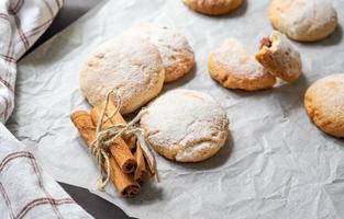 Round apple cookies and string tied cinnamon sticks on greaseproof baking paper photo
