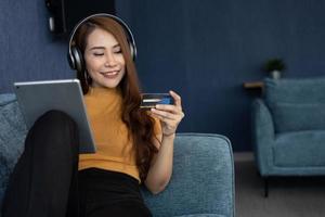 Portrait of young woman wear headphones and holding tablet and banking credit card, transferring money online, shopping goods in internet store, purchasing services, satisfied with secure payments. photo