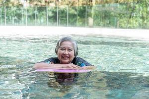 Young trainer helping senior woman in aqua aerobics and working out in the pool. old woman and mature man doing aqua aerobics exercise in swimming pool, Elderly sports, and active lifestyle concept. photo