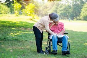 Senior couple in the park and wife taking care of a husband in a wheelchair a patient with paralysis, with his wife comforting and encouraging each other. Retirement health insurance concept. photo