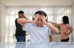 Asian boy kid wearing headphones and play loud music. so as not to hear quarrel while parents having fight or quarrel conflict at home. Unhappy problem in family, Domestic problems in the family. photo
